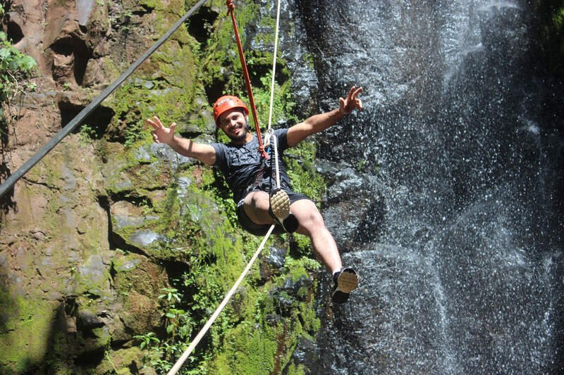 Pessoa fazendo rapel ao lado de uma cachoeira